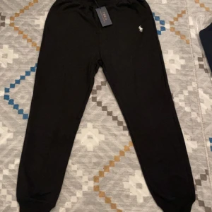 Svarta mjukisbyxor från Ralph Lauren - Snygga svarta mjukisbyxor från Ralph Lauren med det klassiska logotypbroderiet på sidan. Byxorna har en bekväm passform med elastisk midja och muddar vid bensluten. Perfekta för en avslappnad stil.