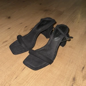 Svarta sandaler med klack - Stilrena svarta sandaler med fyrkantig tå och klack. De har en smal rem över tårna och en justerbar rem runt ankeln. Klacken är 9cm. Passformen är ”wide fit”