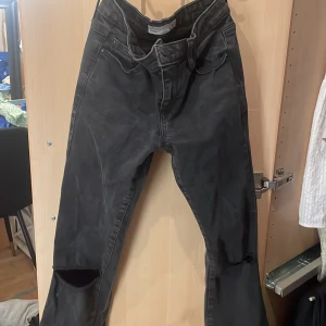 Svarta bootcut jeans - Säljer ett par svarta bootcut jeans i storlek 158. De har en cool sliten look med hål vid knäna. Perfekta för en avslappnad stil.