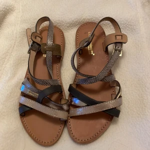 Sandaler från Les Tropeziennes - Snygga sandaler från Les Tropeziennes med flera remmar i olika färger och mönster. De har en elegant design med en mix av svart, beige och ormskinnsmönster. Perfekta för sommardagar.