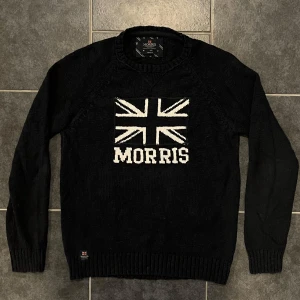 Svart tröja från Morris - Snygg svart tröja från Morris med Union Jack-motiv och texten 'Morris' på framsidan. Tillverkad i 100% bomull för en bekväm känsla. Perfekt för en stilren look.