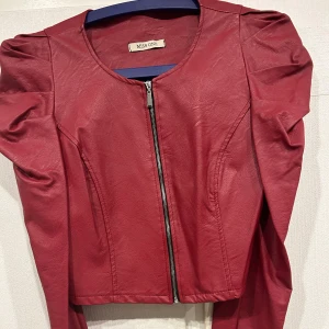 Röd skinnjacka från Miss One - Snygg röd skinnjacka från Miss One med dragkedja framtill. Jackan har en stilren design med långa ärmar och en rund halsringning. Perfekt för att ge din outfit en edgy touch. Använd bara en gång.