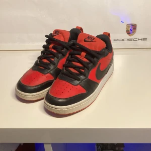 Nike court borough - Snygga Nike sneakers i rött och svart med klassisk design. Skorna har en vit sula och svart snörning, perfekt för en sportig look. Nike-loggan syns tydligt på sidan och hälen.