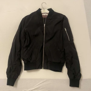 Svart bomberjacka från Stay - Snygg svart bomberjacka från Stay med dragkedja framtill och en ficka med dragkedja på ärmen. Jackan har ribbade muddar vid ärmslut och nederkant för en klassisk look.