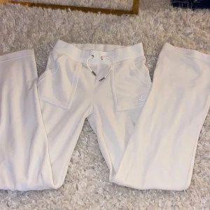 Vita mjukisbyxor från Juicy Couture - Säljer ett par vita mjukisbyxor från Juicy Couture med snörning i midjan och broderad logga på framsidan. Byxorna har praktiska fickor både fram och bak med knappar. Perfekta för en avslappnad stil. De är i väldigt bra skick! Kan passa för personer med storlek S och vanlig XS!! Hör av er för ett par underbara vita Juicy Couture byxor!! OBS PRISET KAN DISKUTERAS 