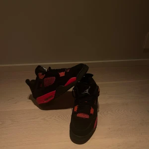 Jordan 4s. Svarta och röda sneakers från Nike - Snygga svarta sneakers med röda detaljer från Nike. Skorna har en ikonisk design med snörning och vit logotyp på tungan. Perfekta för en sportig look.