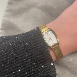 Guldfärgad klocka från Lorus - Elegant guldfärgad klocka från Lorus med en stilren vit urtavla och guldfärgade visare. Klockan har ett mesh-armband i guld och en rektangulär boett. Perfekt för att ge en touch av lyx till din stil.