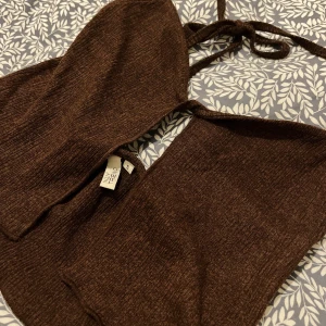 Brun ribbad topp - Brun ribbad topp i en snygg brun färg. Köpt från NLY trend. Toppen har en öppen rygg och knytband i nacken. Den är inte använd alls och är alltså i nyskick. Storlek S.