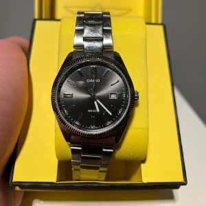 Silverfärgad klocka från Casio - Snygg och stilren klocka från Casio med silverfärgad metallarmband och svart urtavla. Klockan har datumvisning och är vattentålig upp till 50 meter. Perfekt för både vardag och speciella tillfällen. Den är 36mm. Finns extra länkar till för att förstöra den