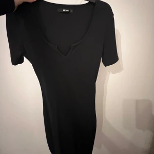 Svart ribbad klänning från Bik Bok - Snygg svart ribbad klänning från Bik Bok med v-ringning. Perfekt för en stilren look. Klänningen har korta ärmar och en figurnära passform. Använd 2 gånger!!!