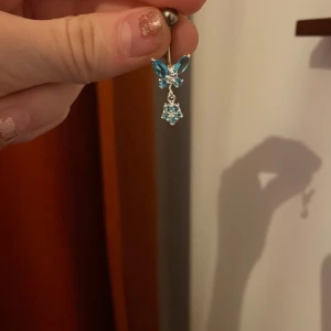 Blått navelpiercingsmycke med kristaller - Snyggt navelpiercingsmycke med blå kristaller i form av blommor och en hängande detalj. Perfekt för att ge en glittrig touch till din stil. 💙