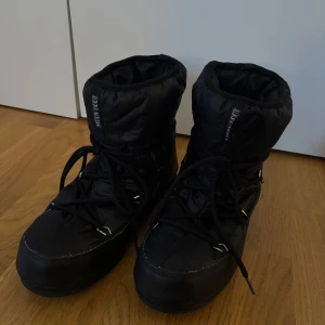 Svarta Moon Boot med snörning - Säljer ett par svarta Moon Boot med snörning. Perfekta för vintern med sin robusta design och varma foder. Sulan har bra grepp för hala underlag. Passar utmärkt för kalla dagar. Påminner om Inuikii designen! Använda i 2 veckor max! Nypris: 2 300kr