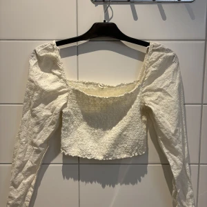 Vit blus med puffärmar - Säljer en söt vit blus med puffiga långärmar och en croppad design. Blusen har en fyrkantig urringning och ett elastiskt parti vid bysten för en bekväm passform. Perfekt för en stilren och trendig look.