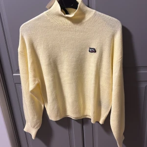 Gul stickad tröja med H&Mmärke - Säljer en ljusgul stickad tröja med hög krage och ett litet H&Mmärke på bröstet. Tröjan har långa ärmar och ribbade kanter som ger en skön passform. Perfekt för kyligare dagar!