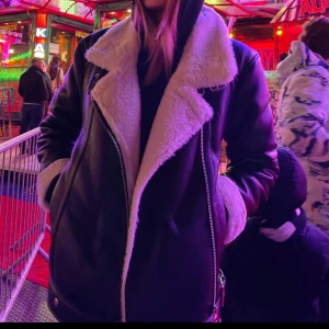 Svart skinnjacka med vit päls - Snygg svart skinnjacka med vit pälsdetalj på kragen och insidan. Jackan har dragkedja och långa ärmar, perfekt för kyligare dagar. En stilren och trendig jacka som passar till många olika outfits.