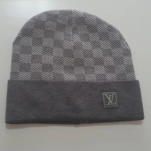 Grå rutig mössa från Louis Vuitton - Snygg grå rutig mössa från Louis Vuitton med uppvikt kant och diskret LV-logga. Perfekt för att hålla värmen med stil under kyliga dagar.