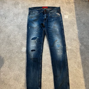 Blå jeans från Replay - Säljer ett par snygga blå jeans från Replay med slitna detaljer och en slim passform, jeansen har ett litet hål vid foten på baksidan, hålet syns INTE med skor på. Hör av dig vid funderingar.  Pris kan diskuteras 
