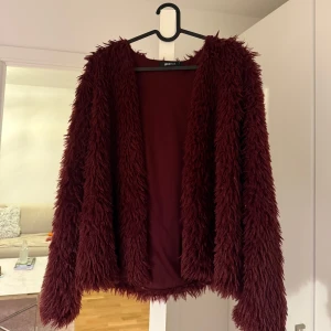 Vinröd pälsjacka från Gina Tricot - Säljer en vinröd pälsjacka från Gina Tricot. Jackan har en fluffig och mysig design med långa ärmar. Perfekt för att hålla sig varm under kyliga dagar.