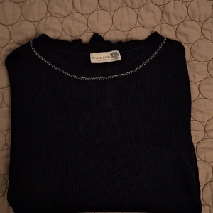 Mörkblå stickad tröja från Dal Lago - Säljer en stilren mörkblå stickad tröja från Dal Lago, tillverkad i Italien. Tröjan har långa ärmar och en rund halsringning med dekorativa vita sömmar. Perfekt för kyligare dagar.