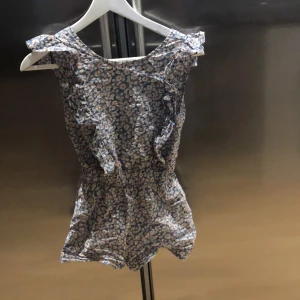 Blommig ärmlös klänning med shorts  - Charmig ärmlös klänning med shorts imed ett blommigt mönster i blått och vitt. Klänningen har volangdetaljer vid axlarna och en smickrande passform. Perfekt för varma sommardagar.