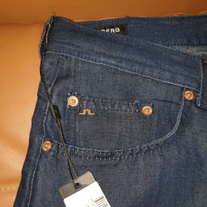 Helt nya jeans från J.Lindeberg - Helt nya mörkblå jeans från J.Lindeberg med klassisk femficksdesign och knappgylf. Perfekta för en stilren look. Org pris ligger runt 1200 kr.