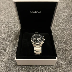 Klocka från Seiko -  Klocka från Seiko. Klockan har en metallarmband och en detaljerad urtavla med flera funktioner. Levereras i originalförpackning med tillbehör och manual.