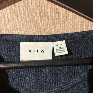 Mörkblå tröja från VILA - Säljer en stilren mörkblå tröja från VILA. Tröjan har en v-ringad hals och långa ärmar med ribbade muddar. 
