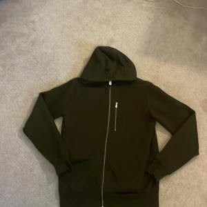 Olivgrön huvtröja från Sail Racing - Snygg olivgrön huvtröja från Sail Racing med dragkedja och en praktisk bröstficka. Perfekt för en casual look med sin stilrena design och bekväma passform. Jag köpte den för runt 1250 och säljer den för att jag inte använder den längre🫒