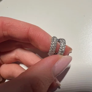 Glittriga silverörhängen - Snygga och eleganta örhängen i silver med glittrande stenar. Perfekta för att ge en extra touch av glamour till din outfit. De är runda och har en stilren design som passar till många tillfällen.