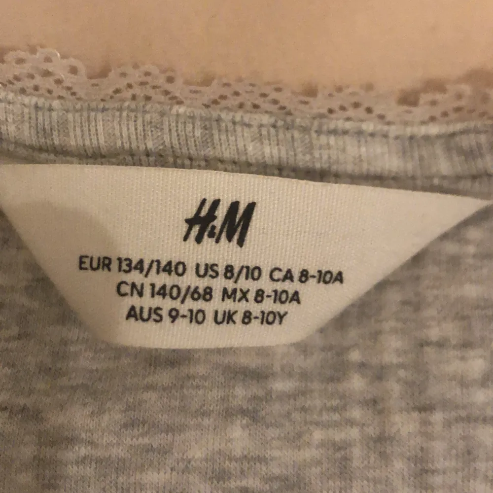 Säljer en grå ribbad topp från H&M med lång ärm och rund halsringning. Perfekt för en avslappnad stil. Toppen är i storlek 134/140 och har en mjuk och bekväm känsla.. Yläosat.