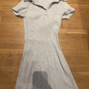 Grå ribbad klänning från Divided - Säljer en stilren grå ribbad klänning från Divided. Klänningen har korta ärmar och en v-ringad krage som ger en elegant touch. Perfekt för både vardag och speciella tillfällen. Passar dig som gillar en enkel men chic stil.