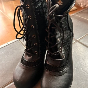 Svarta ankelboots från Demonia! - Svarta rockiga ankelboots med snygga detaljer, snörning fram och dragkedja på insidan från Demonia i storlek 41. Klacken är 6 cm hög och dom är aldrig använda. 