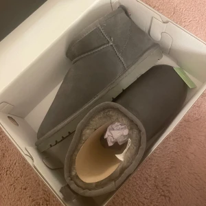 Grå boots med foder - Säljer ett par sprillans nya grå uggs med mjukt foder. Aldrig använt och Perfekta för kyliga dagar med sin bekväma passform och stilrena design. De är lätta att ta på och av, vilket gör dem praktiska för vardagsbruk.