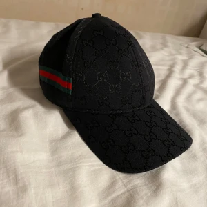 Keps - En svart keps med röd svart band på sidan och en skön design med bokstäverna GG. Pris kan diskuteras vid köp tillsammans med en av mina väskor.