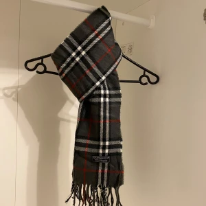Burberry - Säljer nu denna Snygga halsduk från Burberry i färgen grå. Tillverkad i mjukt lammull med klassiskt fransad kant. Perfekt för att hålla dig varm och stilren under kyliga dagar. Hör av er vid funderingar☺️