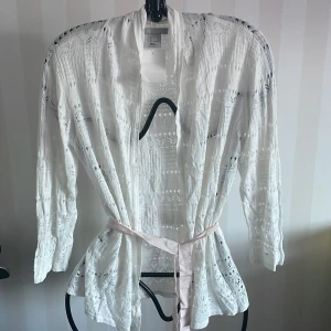 Vit spetskofta från H&M - Säljer en elegant vit spetskofta från H&M. Koftan har långa ärmar och ett fint knytband i midjan. Perfekt för att lägga till en romantisk touch till din outfit. 💫