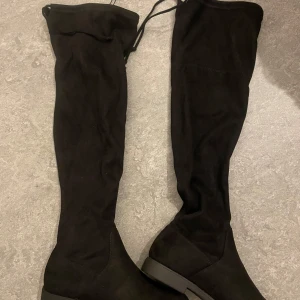 Svarta overknee stövlar - Snygga svarta overknee stövlar i mocka med en stilren design. Perfekta för att ge en elegant touch till din outfit. De har en diskret snörning baktill för justerbar passform. Köpte här på Plick men var tyvärr för stora. Dom är aldrig använda.