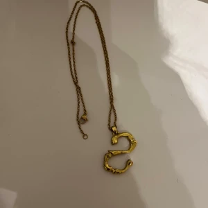 Guldigt halsband med bokstavshänge - Elegant halsband i guld med ett unikt bokstavshänge format som ett 'S'. Kedjan är tunn och smidig, vilket ger en stilren look. Perfekt för att lägga till en personlig touch till din outfit. Lite sliten på ena sidan som syns på bilden men inget man tänker på!💕