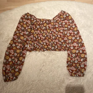 Blommig topp från Hollister - Säljer en söt blommig topp från Hollister. Toppen har långa ärmar och ett färgglatt mönster i rött, gult, rosa och grönt. Perfekt för en bohemisk look!