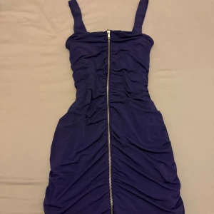 Mörklila klänning med dragkedja - Snygg mörklila klänning med dragkedja framtill. Klänningen har en åtsittande passform och breda axelband. Perfekt för en kväll ute eller en speciell tillställning.