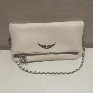 Vit axelväska med kedja - Snygg vit axelväska med en elegant kedja som axelrem. Väskan är använd tre gånger så därav i nyskick. Det tillkommer även en extra kedja som är längre om man vill bära väskan som en crosbody väska.