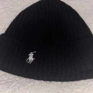 Ralph Lauren Mössa - Knappt använd - Säljer en snygg svart mössa från Ralph Lauren. Köpte den men insåg att den inte riktigt är min stil, så den har mest legat oanvänd. Perfekt för dig som gillar trendig stil