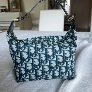 Mönstrad handväska med dragkedja - Säljer en snygg axelväska med ett unikt mönster i blått. Väskan har en praktisk dragkedja och en kort axelrem i mörk lack. Perfekt för att ge din outfit en stilfull touch.