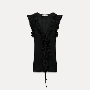 Svart ribbad topp från Zara - Snygg svart ribbad topp från Zara med volangdetaljer och knyt framtill. Den har en v-ringad design och är ärmlös, vilket gör den perfekt för varmare dagar. Oanvänd, ny med prislapp!
