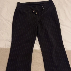 Svarta randiga kostymbyxor - Snygga svarta kostymbyxor med diskreta ränder. Byxorna har en klassisk design med knappar i midjan och en rak passform. Perfekta för en stilren look. Bootcut low waist pass from köpta från beyond retro