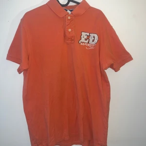 Orange kortärmad t-shirt från Ed Hardy - Säljer en cool orange t-shirt från Ed Hardy med korta ärmar och en unik design. T-shirten har ett stort tryck på baksidan med en bevingad dödskalle och texten 'New York City'. Perfekt för dig som gillar att sticka ut!