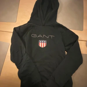 Svart hoodie från GANT - Säljer en stilren svart hoodie från GANT med ett broderat märke på framsidan. Mycket bra skick. Storlek 158/164. Kan hämtas i Skövde eller fraktas mvh Lukas.