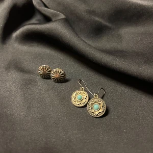 2par Örhängen i silver och turkos - Säljer två par örhängen. Ett par är små och runda i silver med en blomliknande design. Det andra paret är hängande med en turkos sten i mitten, omgiven av en detaljerad silverram. Ej äkta silver