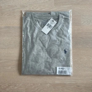 Grå t-shirt från Ralph Lauren - Säljer en stilren grå t-shirt från Ralph Lauren. Perfekt för en avslappnad look. T-shirten är i bomull och kommer i originalförpackning. Alltså helt ny, säljer då den inte passar min smak. Storlek M sitter som den ska! 300 kronor billigare en nypris. 