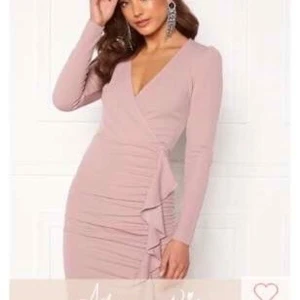 Rosa klänning från Bubbleroom - Säljer en elegant rosa klänning från Bubbleroom med v-ringning och volangdetaljer framtill. Klänningen har långa ärmar och en dragkedja i ryggen. Perfekt för en stilfull look!